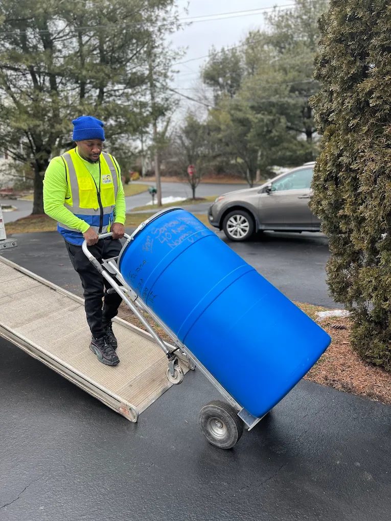 Afford It crew member wheeling a blue shipping barrel down the truck ramp on a hand truck